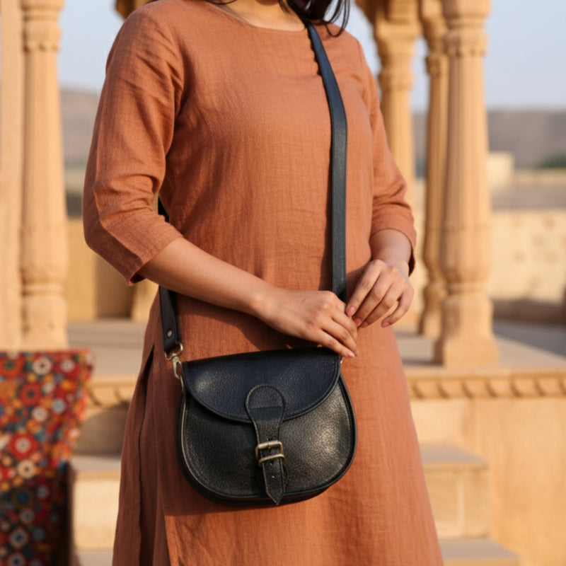 A person wearing a handcrafted Jeengar leather crossbody bag while walking down a historic stone street in Rajasthan.