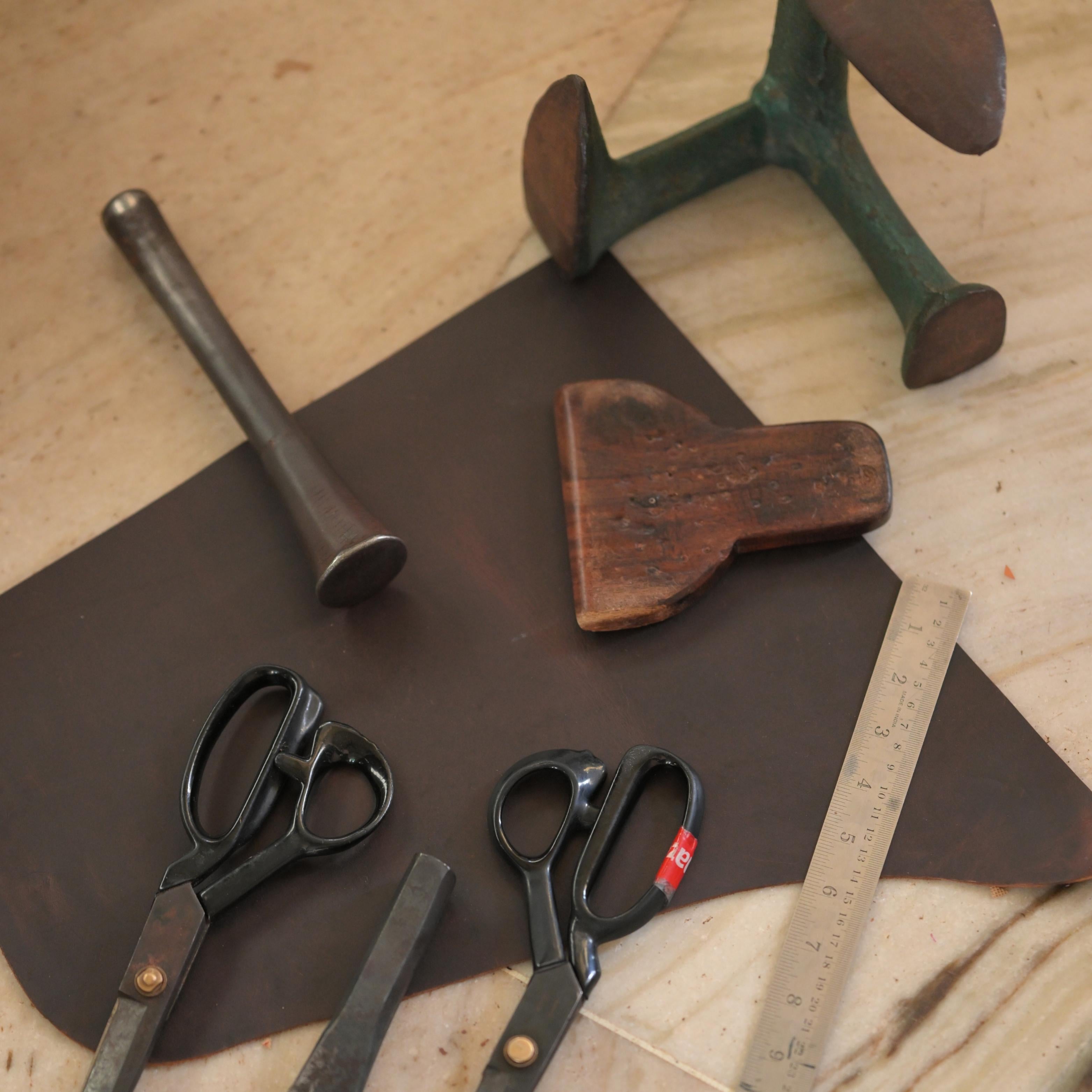 Vintage tools including a hammer, pliers, and scissors on a wooden surface for leather craft.