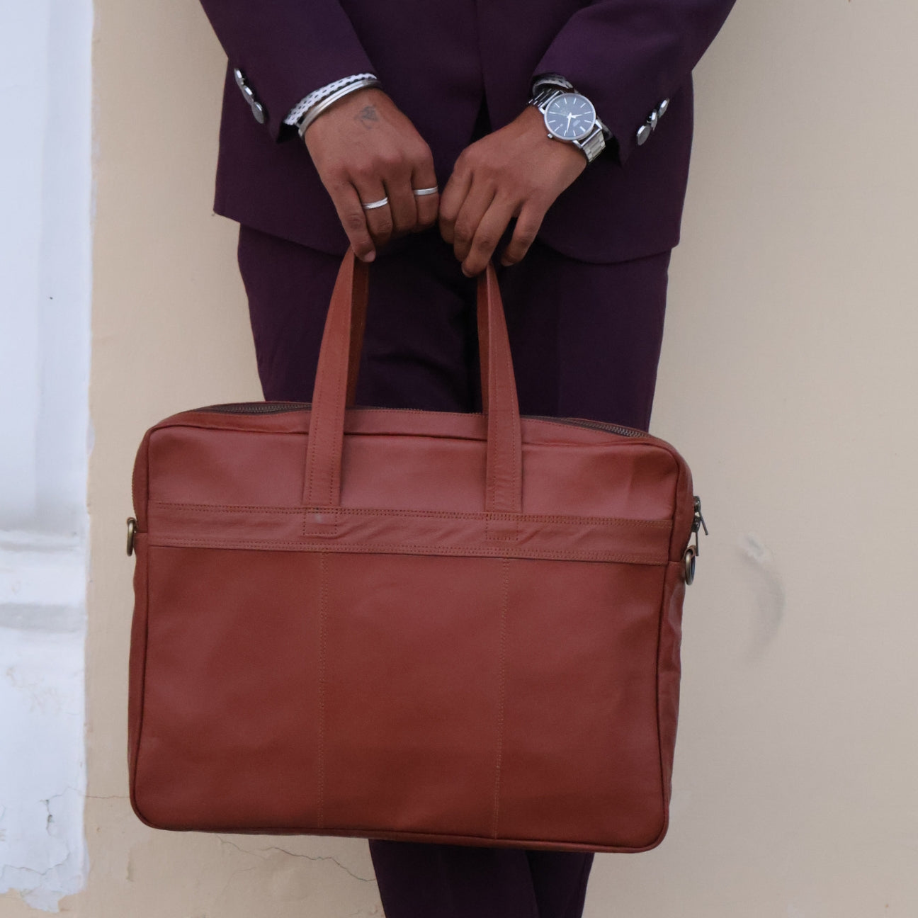 Person holding a brown leather briefcase against a neutral background