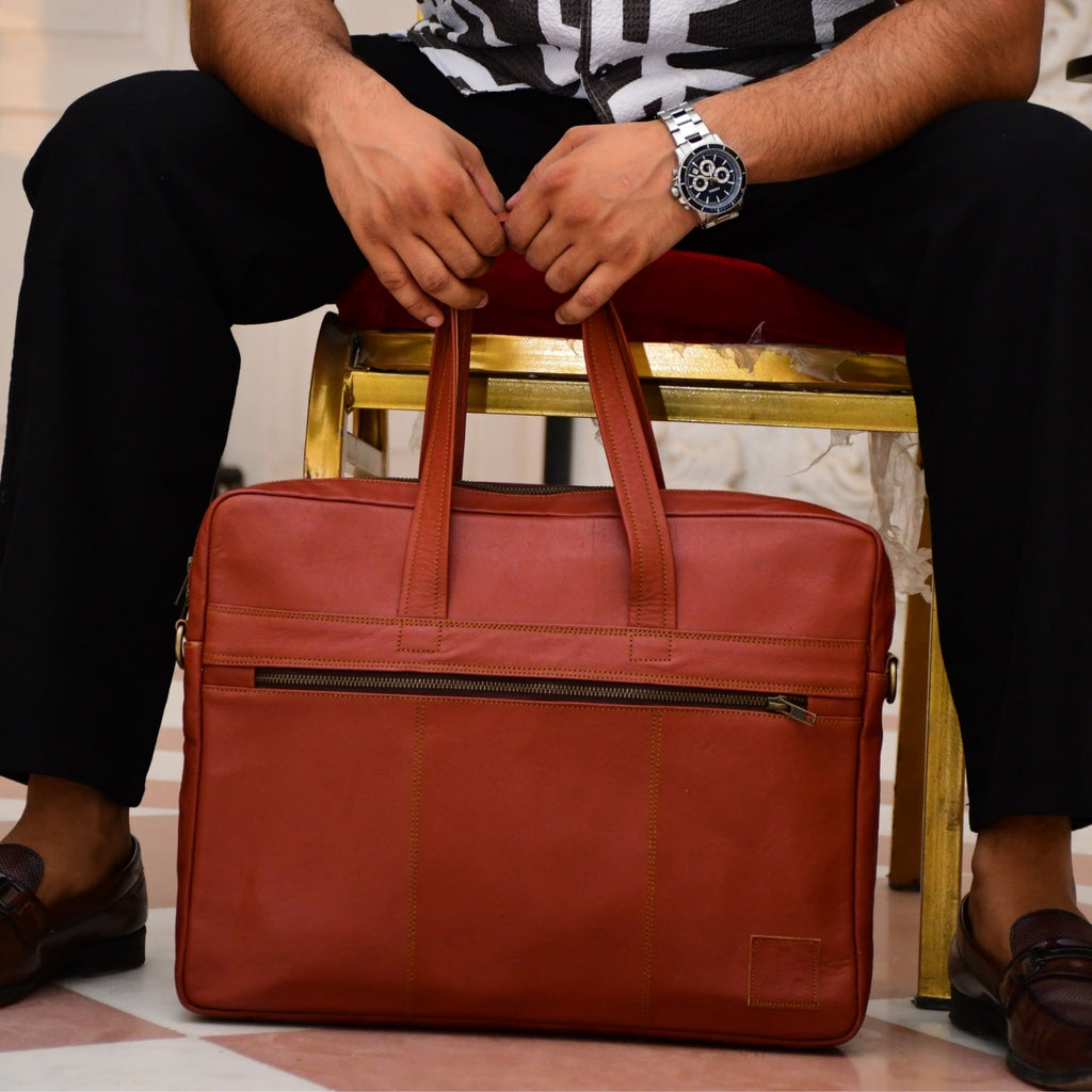 Person holding a brown leather briefcase with a gold chair and patterned floor in the background