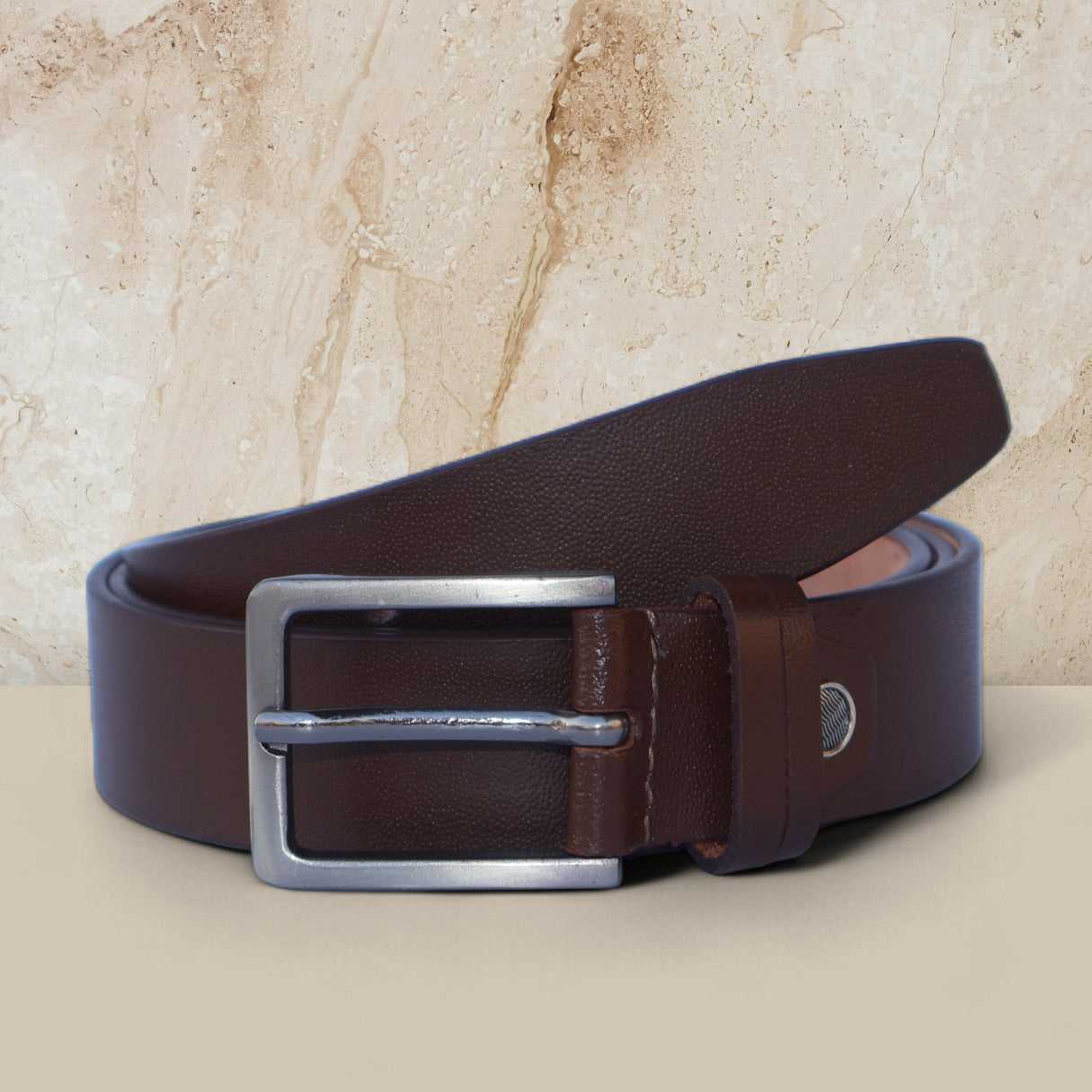 Brown leather belt with silver buckle on a beige surface