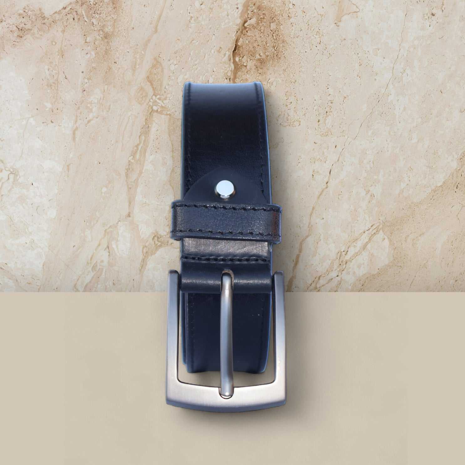 Black leather belt with silver buckle on a beige marble background