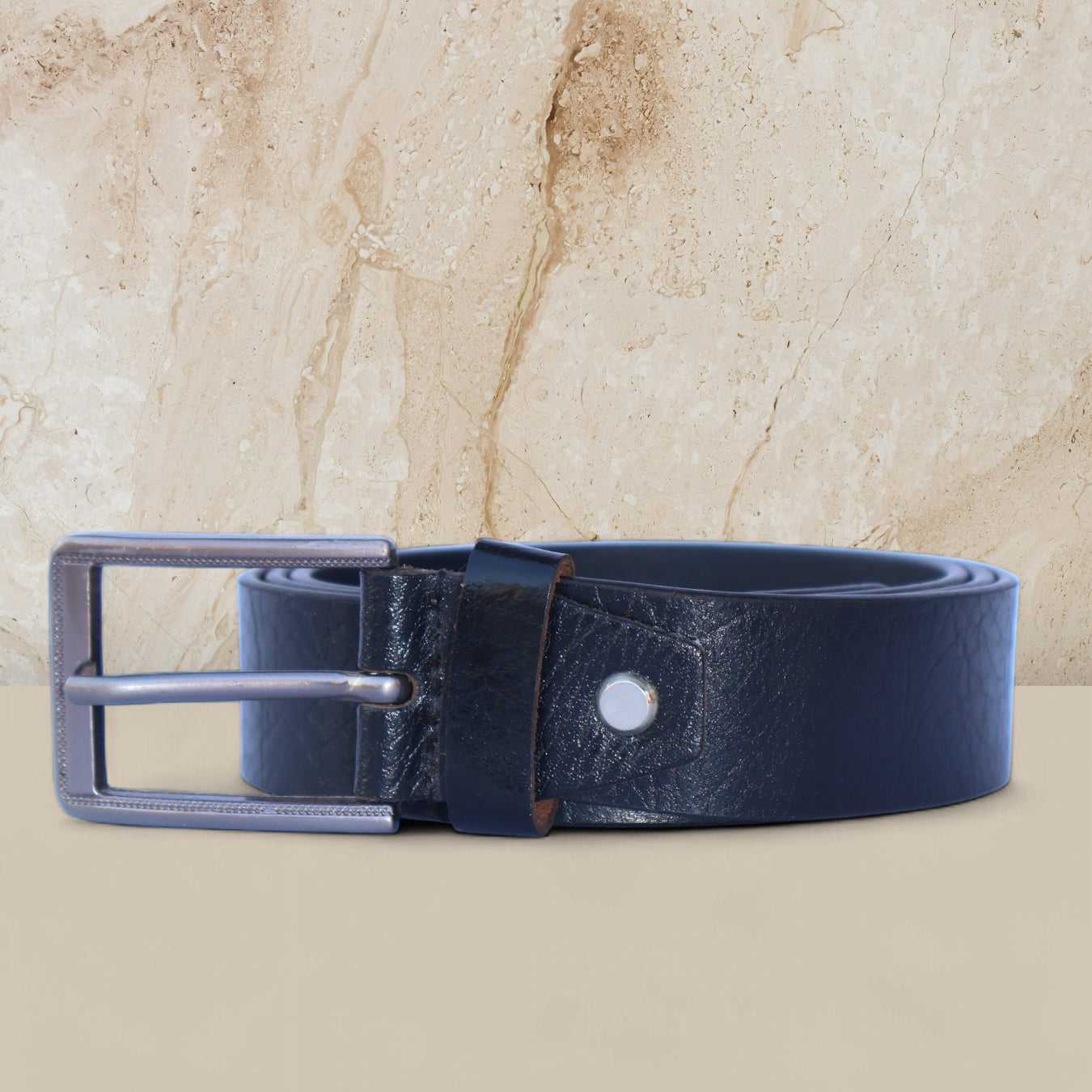 Black leather belt with silver buckle on a beige marble background