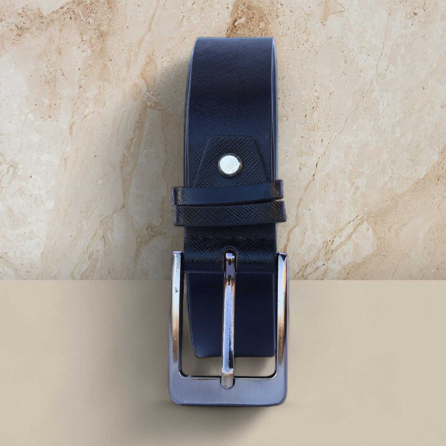 Black leather belt with silver buckle on a beige marble background
