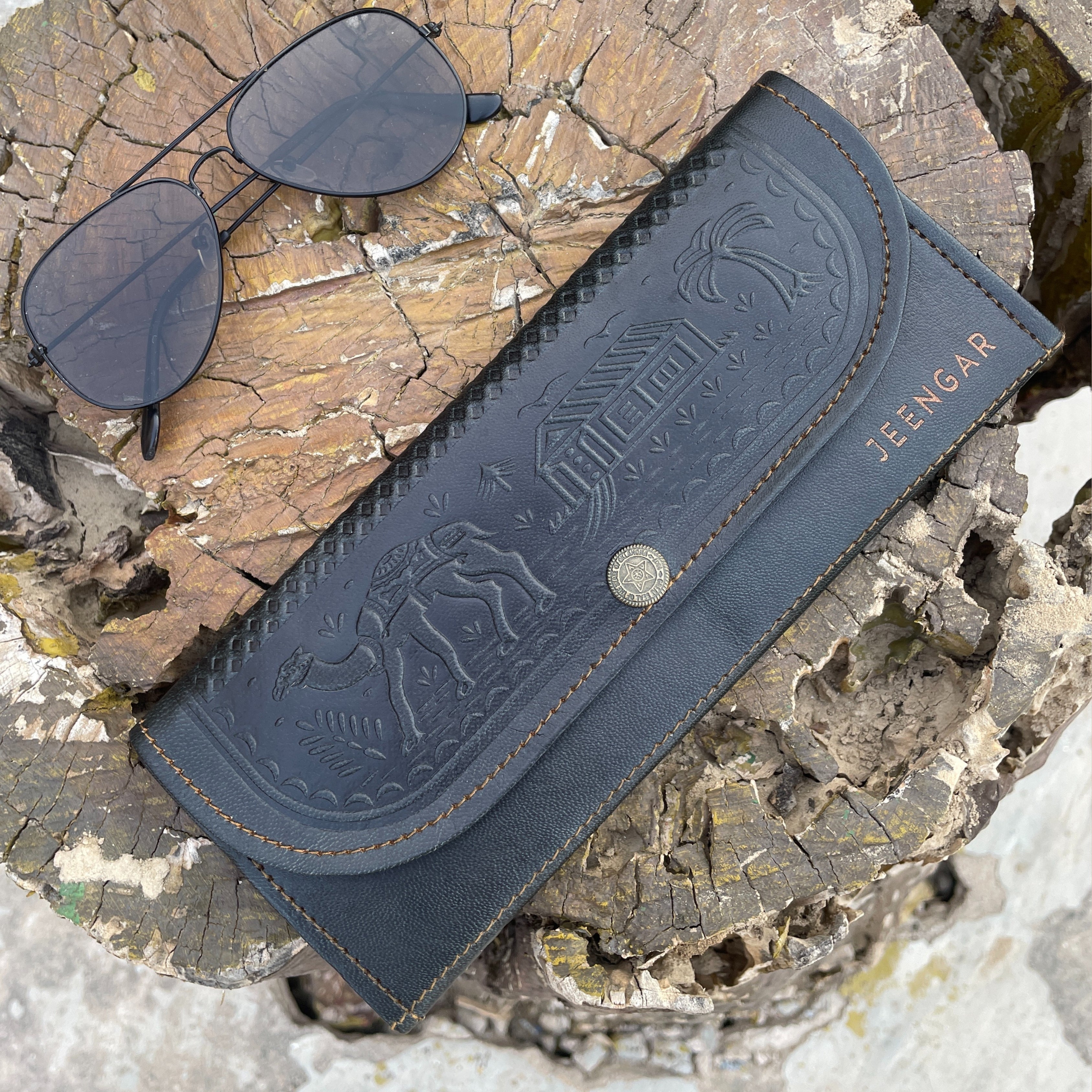 Black sunglasses with an embossed leather clutch on a wooden surface