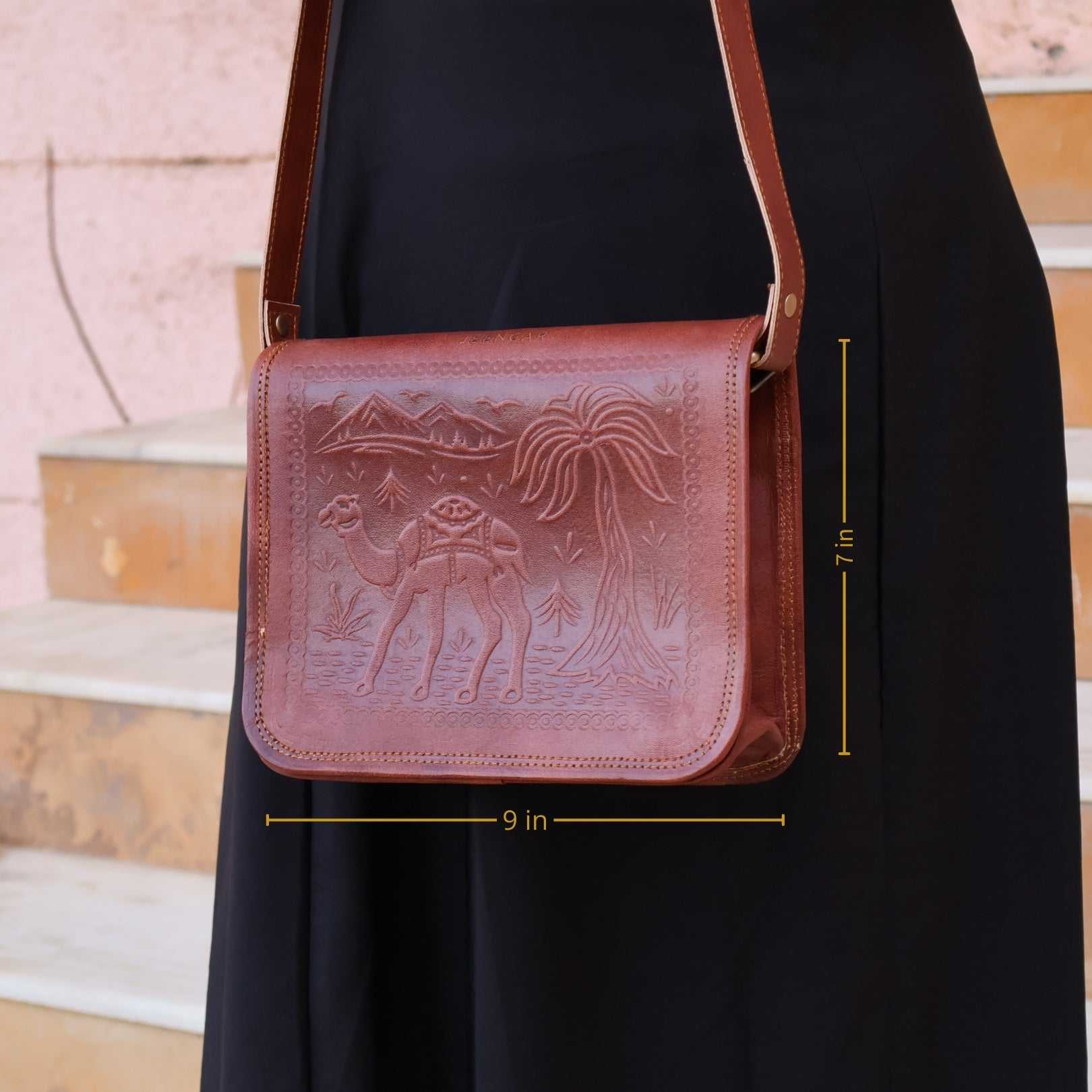 Brown leather bag with embossed design held by a person, with measurements indicated.