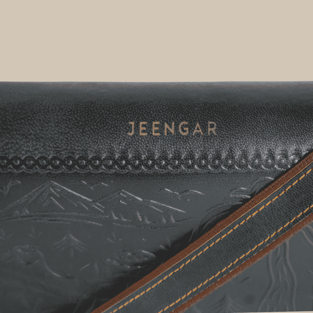 Close-up of a dark green leather bag with 'JEENGAR' branding and mountain embossing.