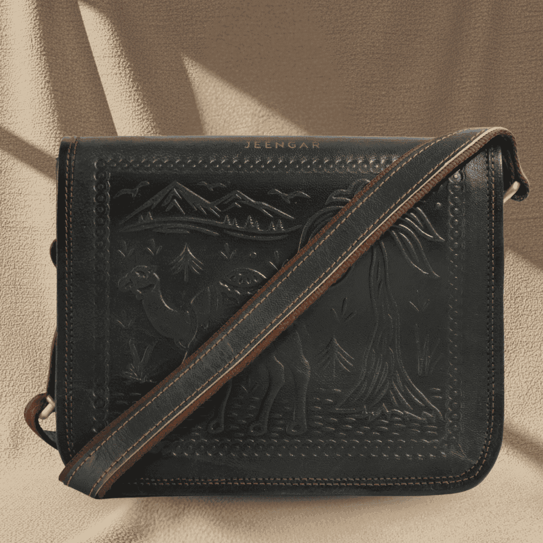 A dark olive green leather bag with embossed designs and brown strap on a beige background