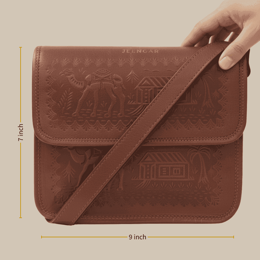 Brown leather bag with embossed designs held by a hand, with measurements indicated.