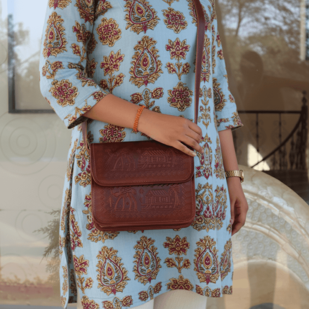 Person wearing a patterned dress holding a cherry leather bag outdoors.