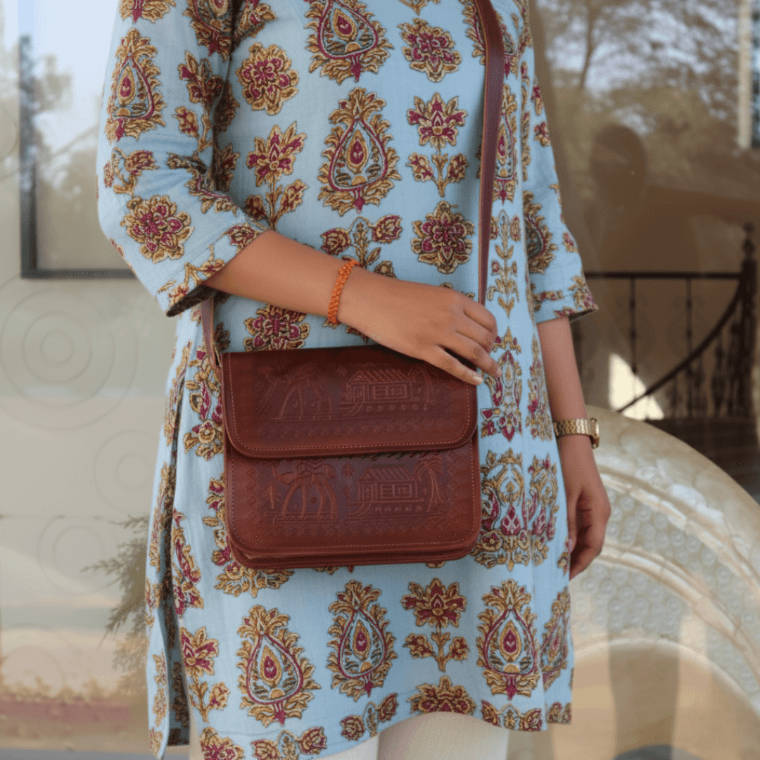 Person wearing a patterned dress holding a cherry leather bag outdoors.