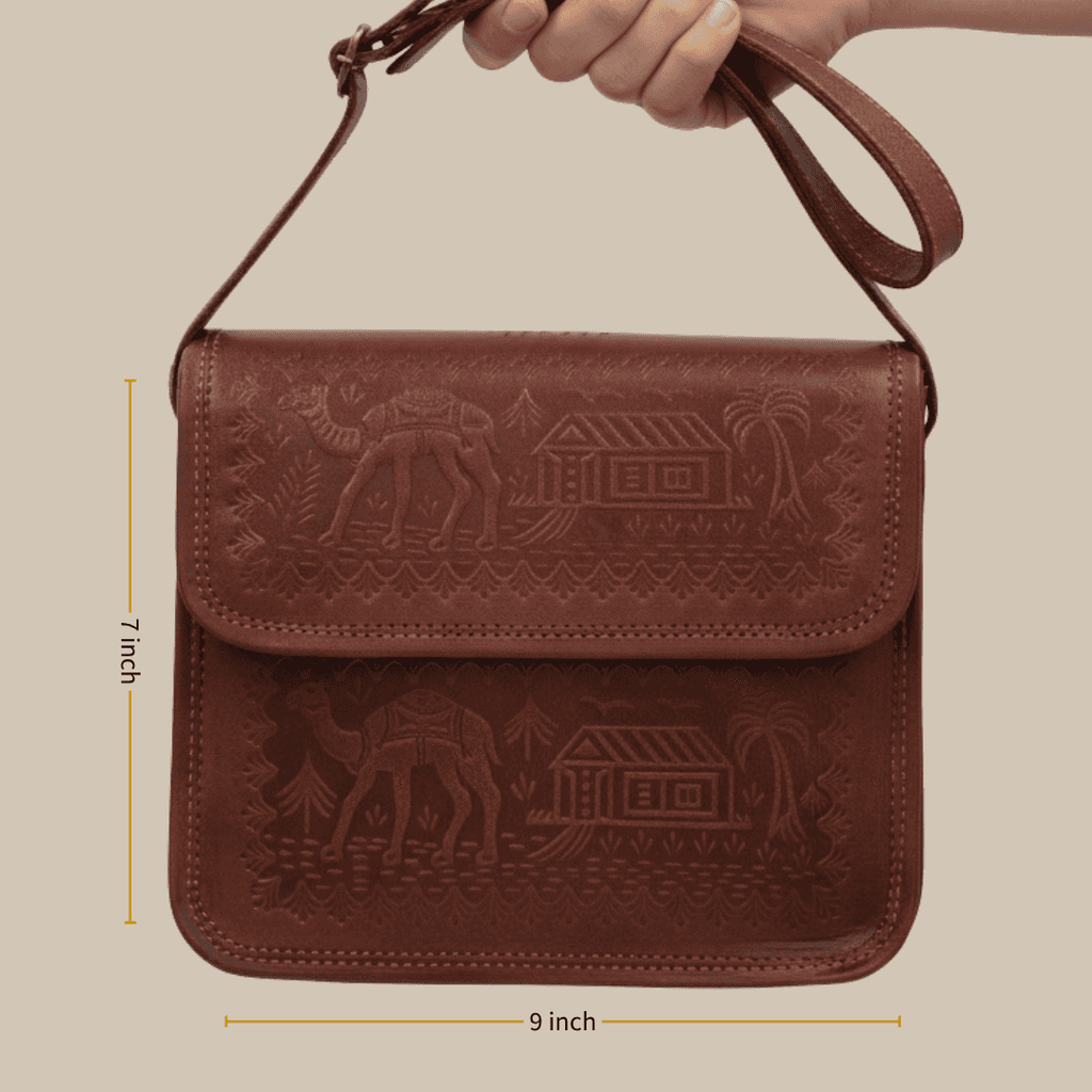 Cherry leather bag with embossed designs held by a hand, with measurements indicated.