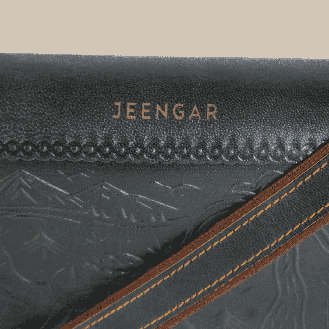 Close-up of a dark green leather product with 'JEENGAR' branding and mountain embossing.