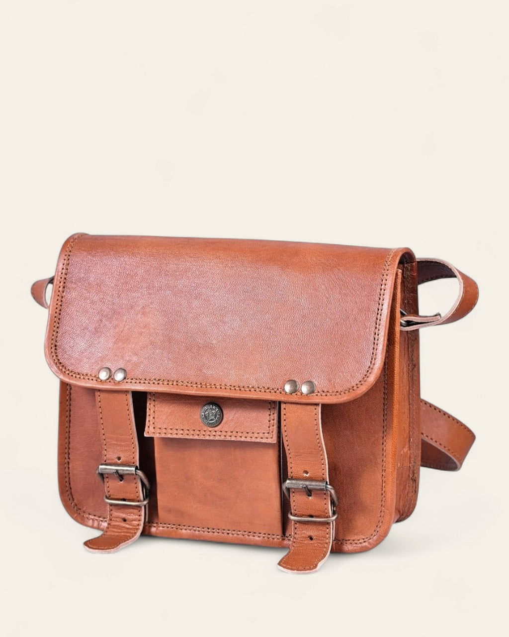 The Jaigarh Sling in natural certified leather, front view with twin buckle straps and antique-brass concho