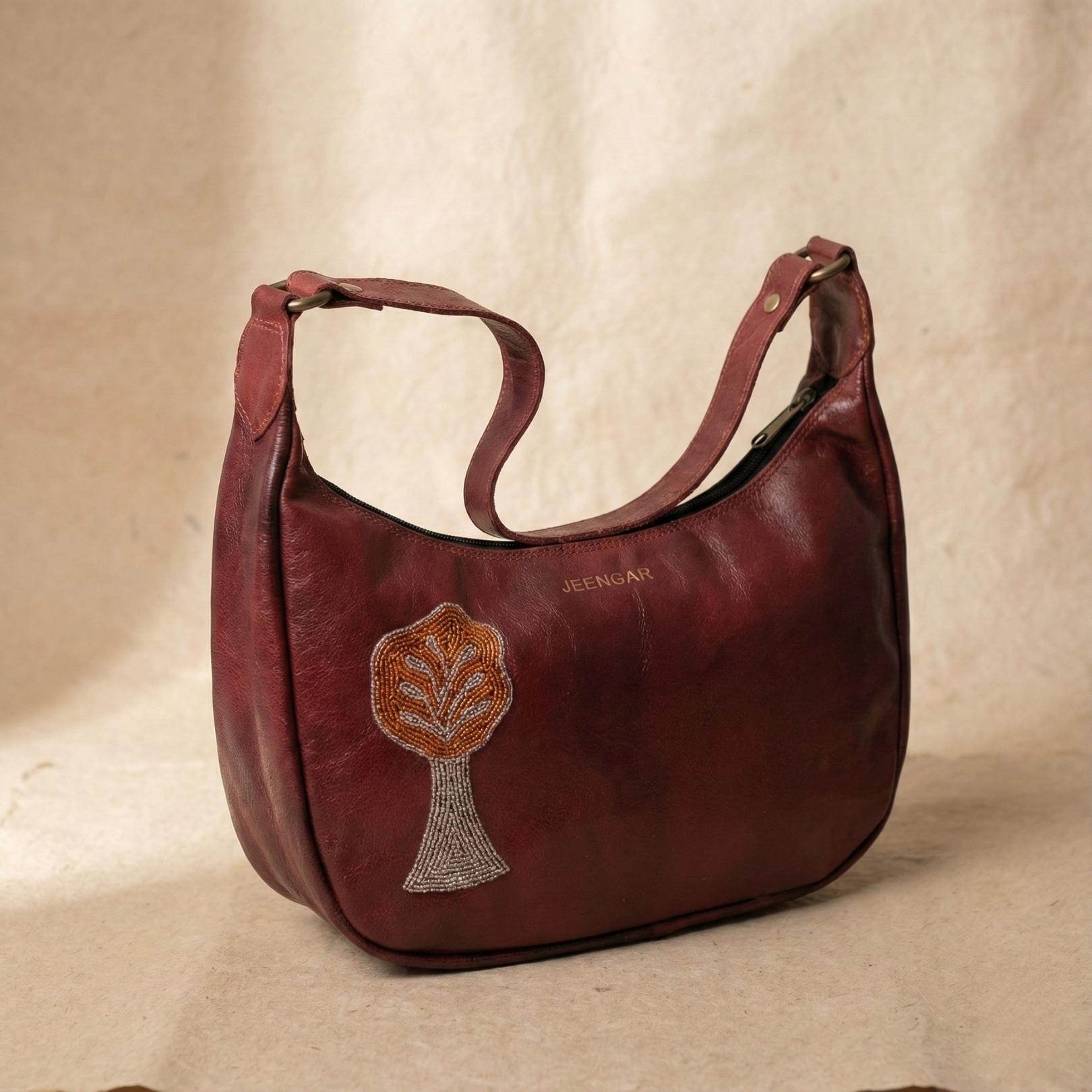 The Padmini Shoulder Bag in cherry top-grain leather, featuring a hand-embroidered Tree of Life.