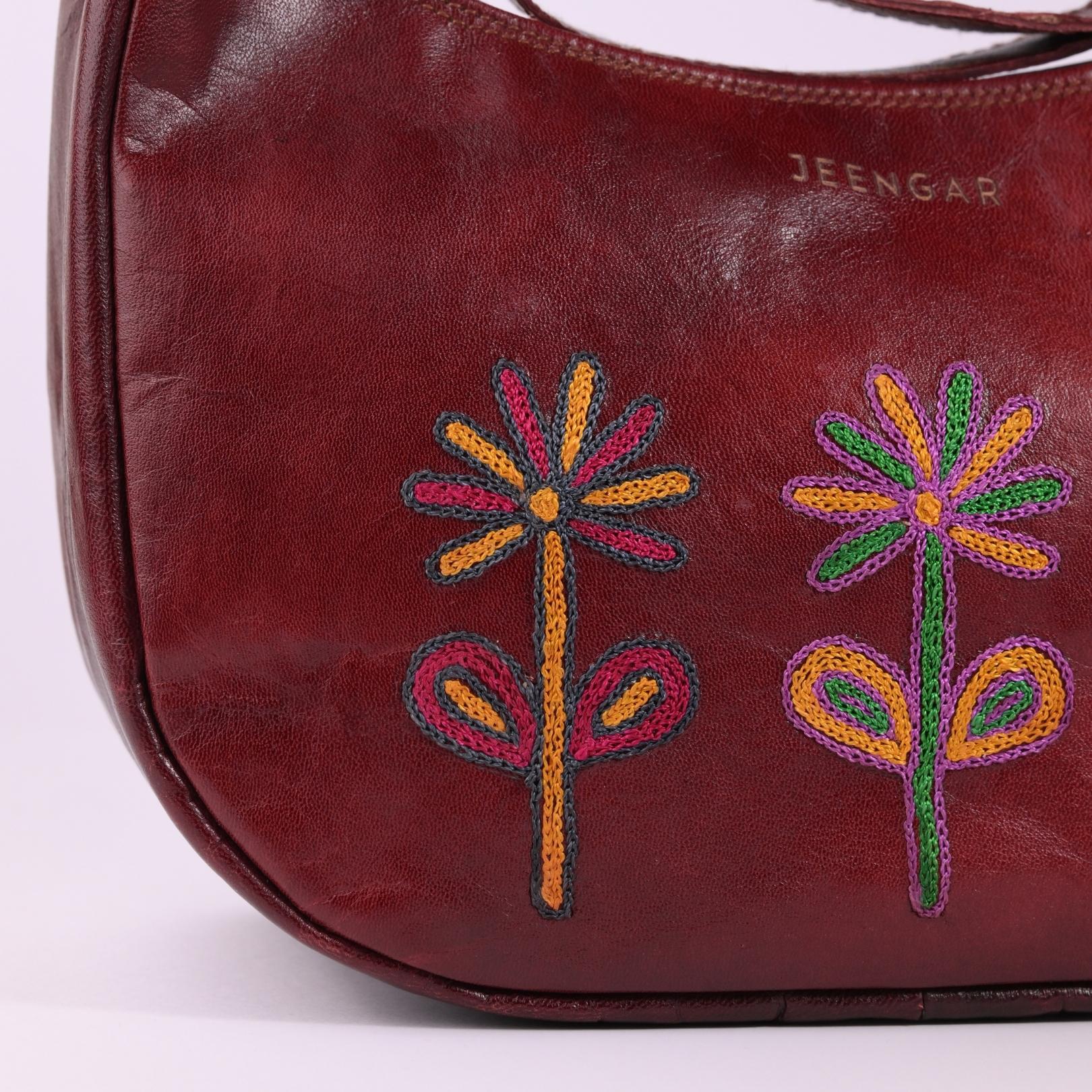 Close-up of the vibrant, hand-embroidered flowers on the Sanyogita leather shoulder bag.