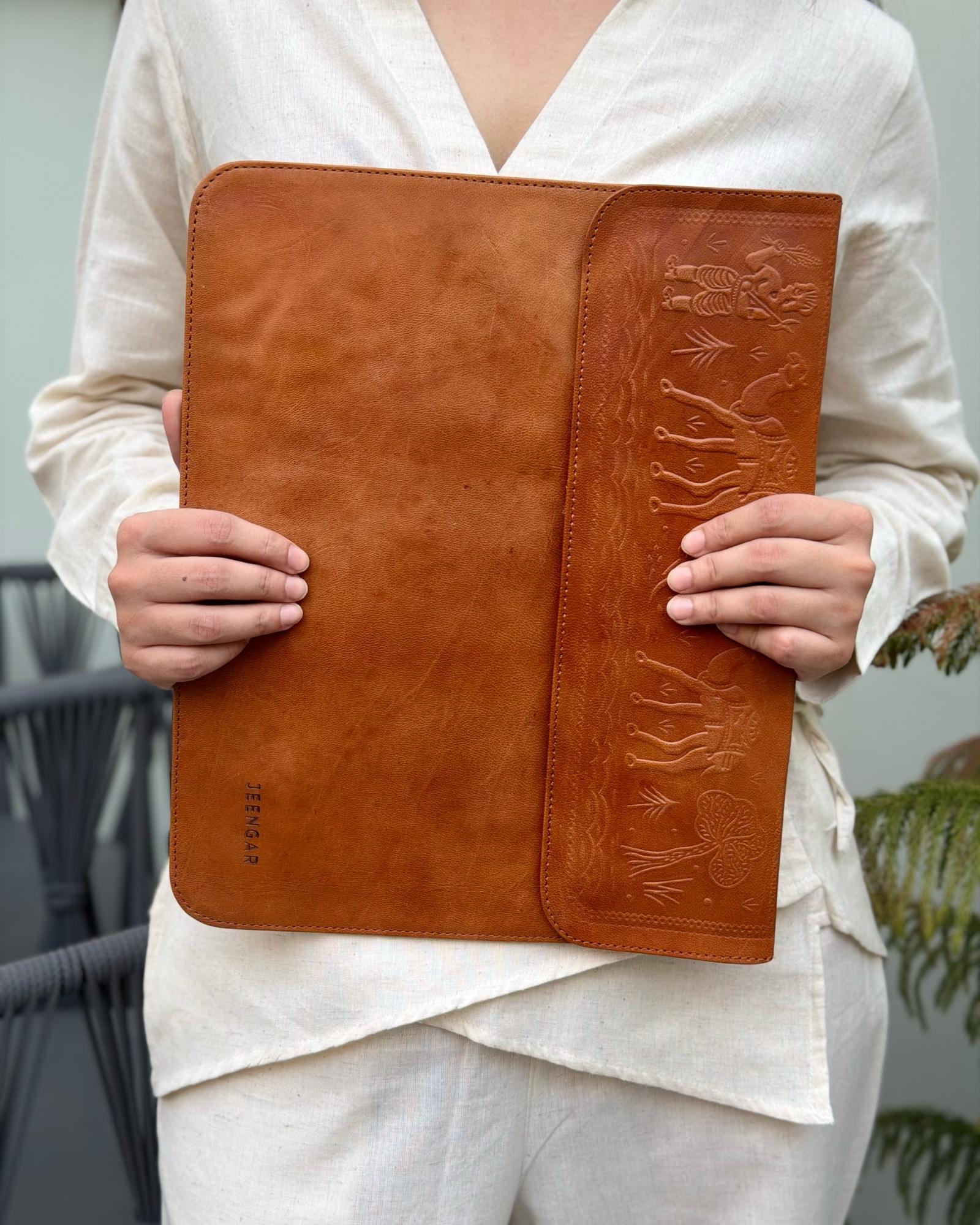 Close-up macro shot of the intricate hand-embossed camel caravan artwork on the flap of The Barmer leather tech sleeve.